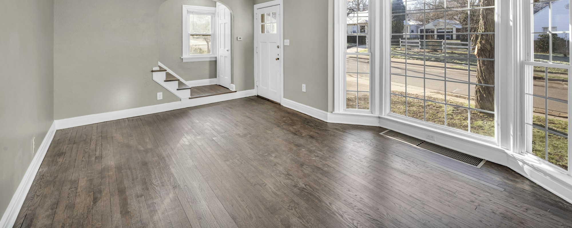 Empty, unfurnished living room with a bay window and bare wooden floor